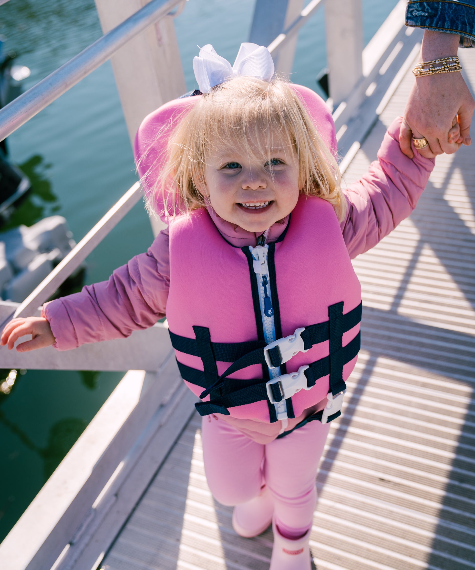 Child in a pink life jacket standing on a dock by water